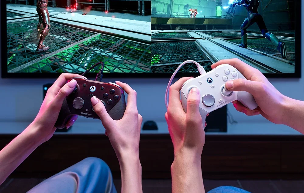 Lähivaade kahe inimese kätele, kes hoiavad teleri ees mängides GameSiri kontrollereid.