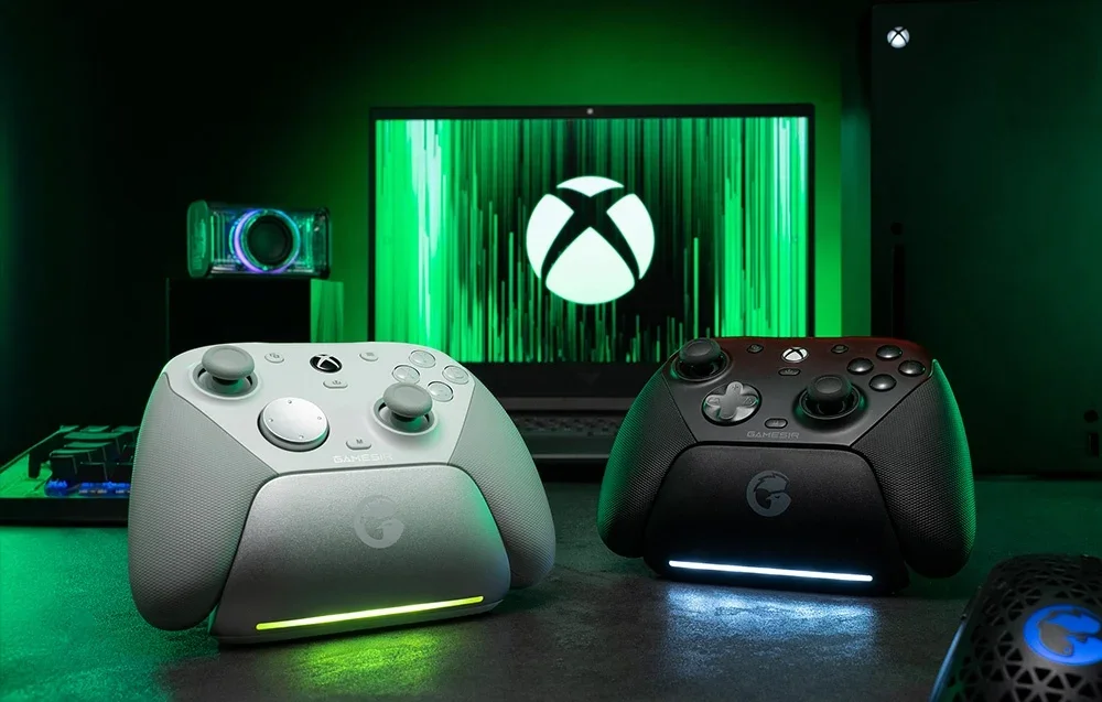 Kaks GameSiri kontrollerit dokis Xboxi logoga monitori ees, üks valge ja teine must.